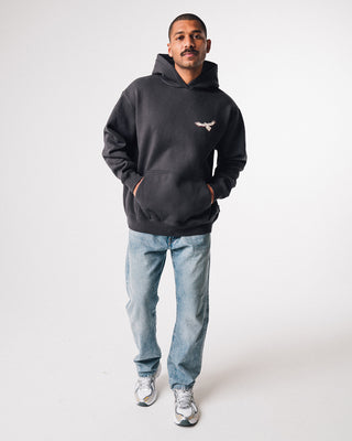 bunjil the wedged-tailed eagle hoodie  in a washed out black color being worn in a full length front image displaying murrundindi eagle logo along with the overall fit of the garment