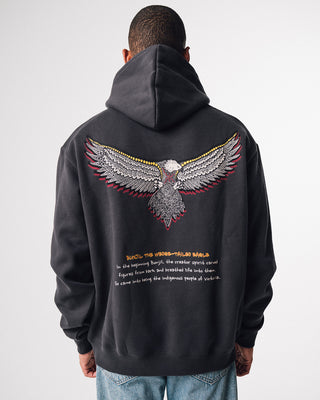 bunjil the wedged-tailed eagle indigenous art on the back of a hoodie in a washed out black color being worn. Text on hoodie below art says 'in the beginning bunjil, the creator spirit carved figures from bark and breathed life into them. so came into being the indigenous people of Victoria.'