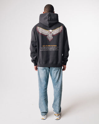 bunjil the wedged-tailed eagle indigenous art on the back of a hoodie in a washed out black color being worn in a full length image. Text on hoodie below art says 'in the beginning bunjil, the creator spirit carved figures from bark and breathed life into them. so came into being the indigenous people of Victoria.'