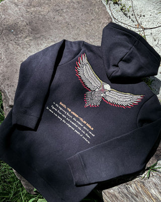 bunjil the wedged-tailed eagle indigenous art on the back of a hoodie placed on a rock to capture details. Text on t-shirt below art says 'in the beginning bunjil, the creator spirit carved figures from bark and breathed life into them. so came into being the indigenous people of Victoria.'