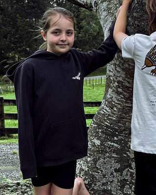 bunjil the wedged-tailed eagle t-shirt being worn in a front full length image displaying murrundindi eagle logo along with overall fit of the hoodie. hoodie is being worn by 8 year old girl in a forest with large trees and bushes