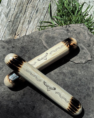 clap sticks indigenous instrument stacked on top of each other on a rock showing details of pine wood and etched burn logo pattern details 