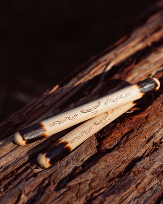 clap sticks indigenous instrument stacked on top of each other on a rock showing details of pine wood and etched burn logo pattern details